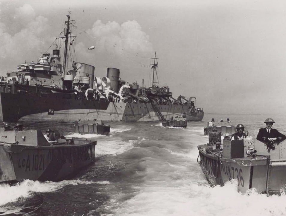A group of small landing craft heading towards the camera, with a large ship in the background