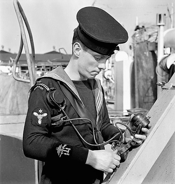Man in a sailor's uniform looking down at equipment he is holding