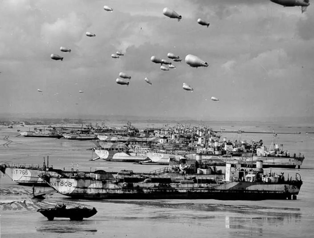Photo looking along a beach with a line of Landing Craft, Tanks seen from the side
