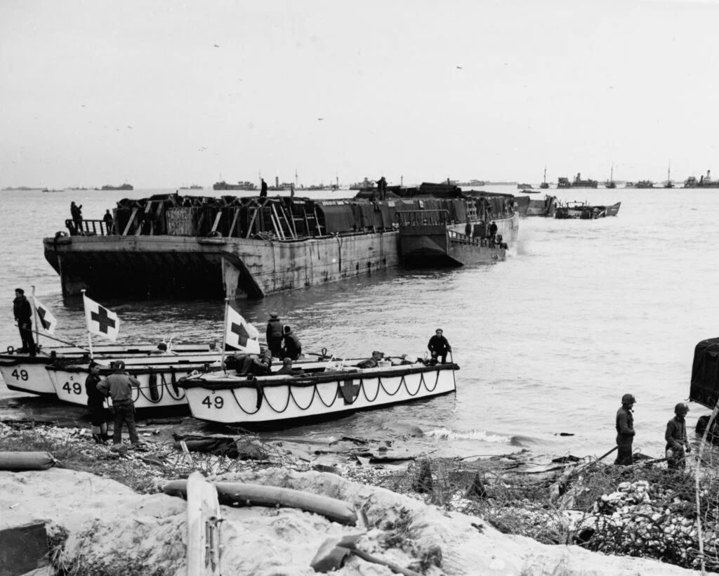 Three small boats at the water's edge, with a larger barge behind them