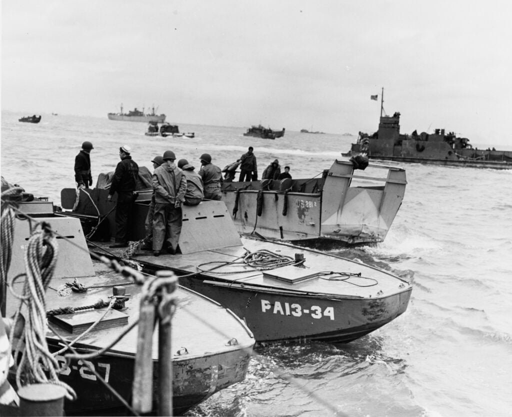 Three small landing craft or boats alongside each other at sea, with more in the distance