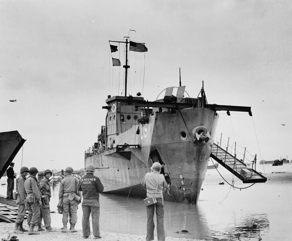 Group of men viewing damaged landing craft on beach